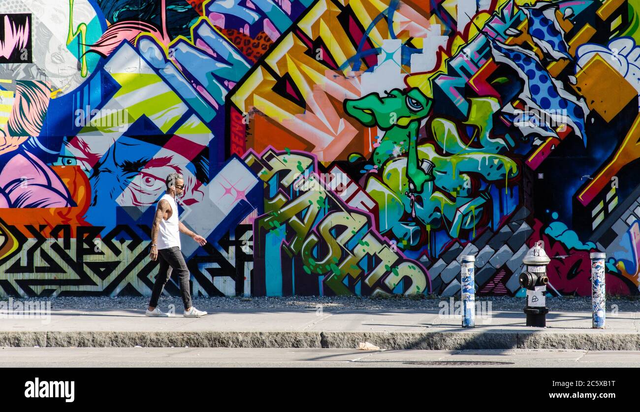 Street art in Brooklyn. Hipster male walking next to a wall of graffiti in Brooklyn, New York, US. Stock Photo