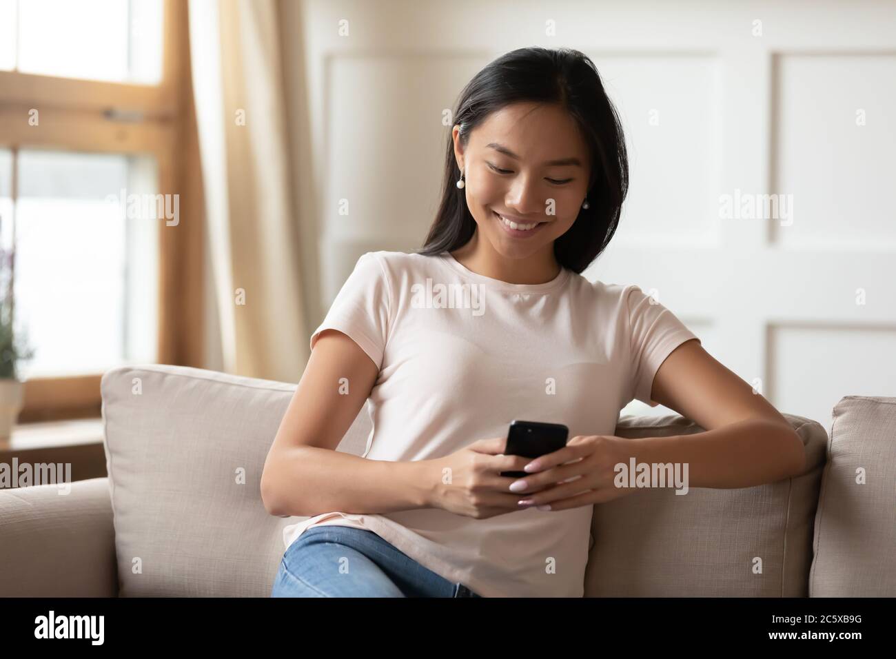 Smiling young vietnamese woman using mobile applications. Stock Photo