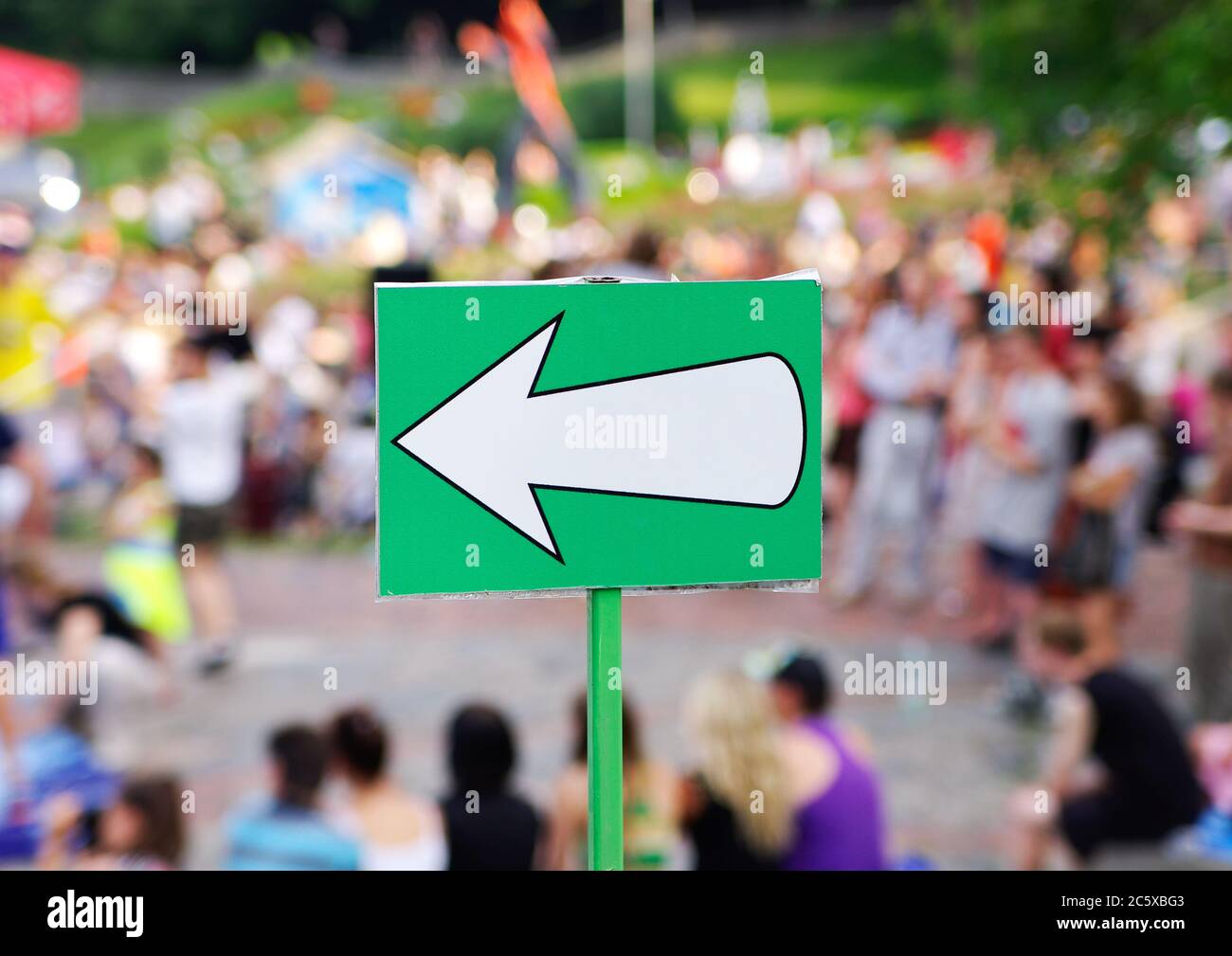 Clear white arrow direction sign against blurred crowd Stock Photo