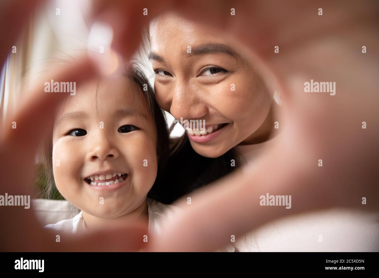 Little asian baby girl making heart gesture with smiling mom. Stock Photo