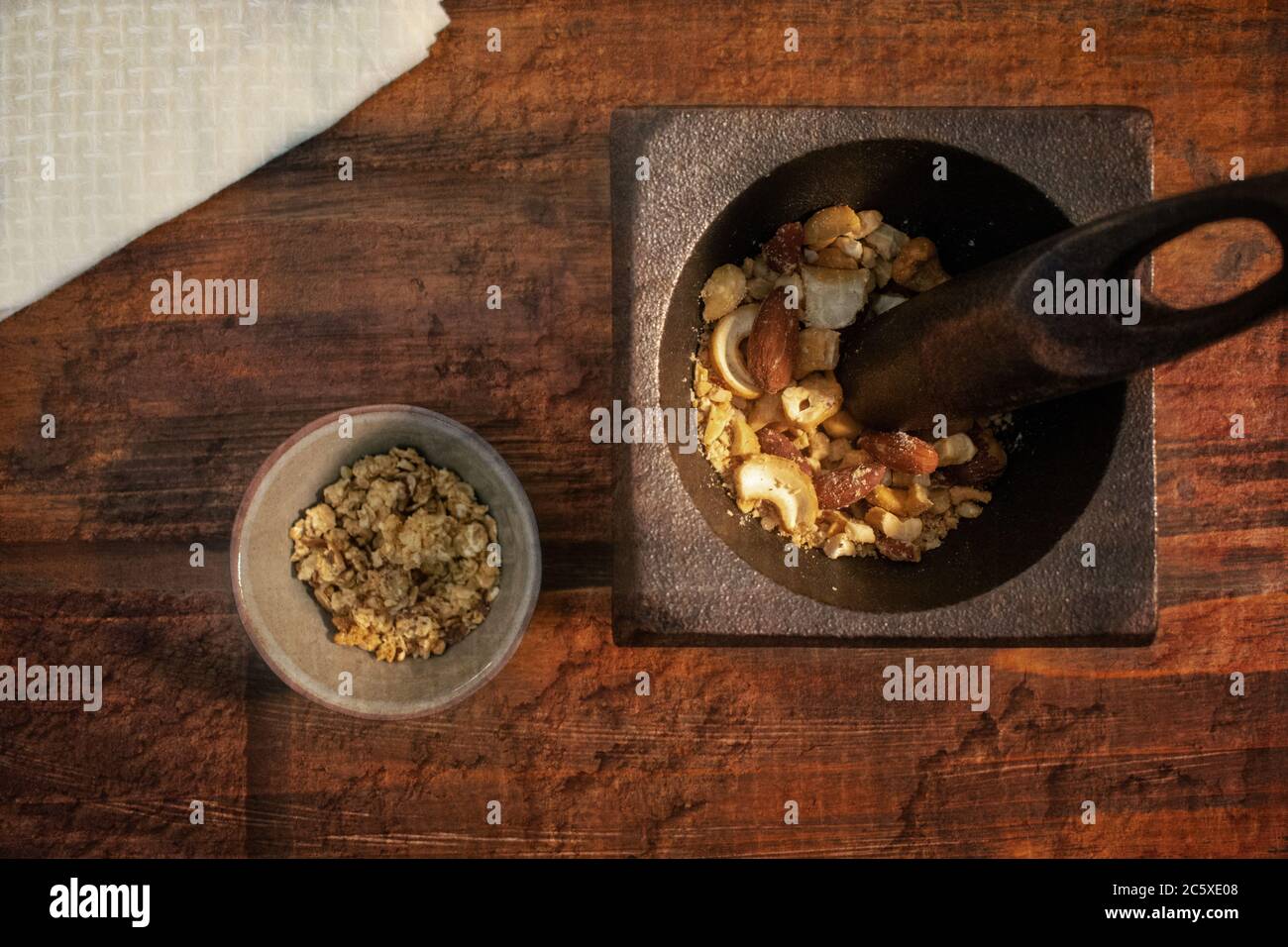 Top view of mixed nuts in mortar with pestle and granola bowl with textured effect background. Still life texture Stock Photo