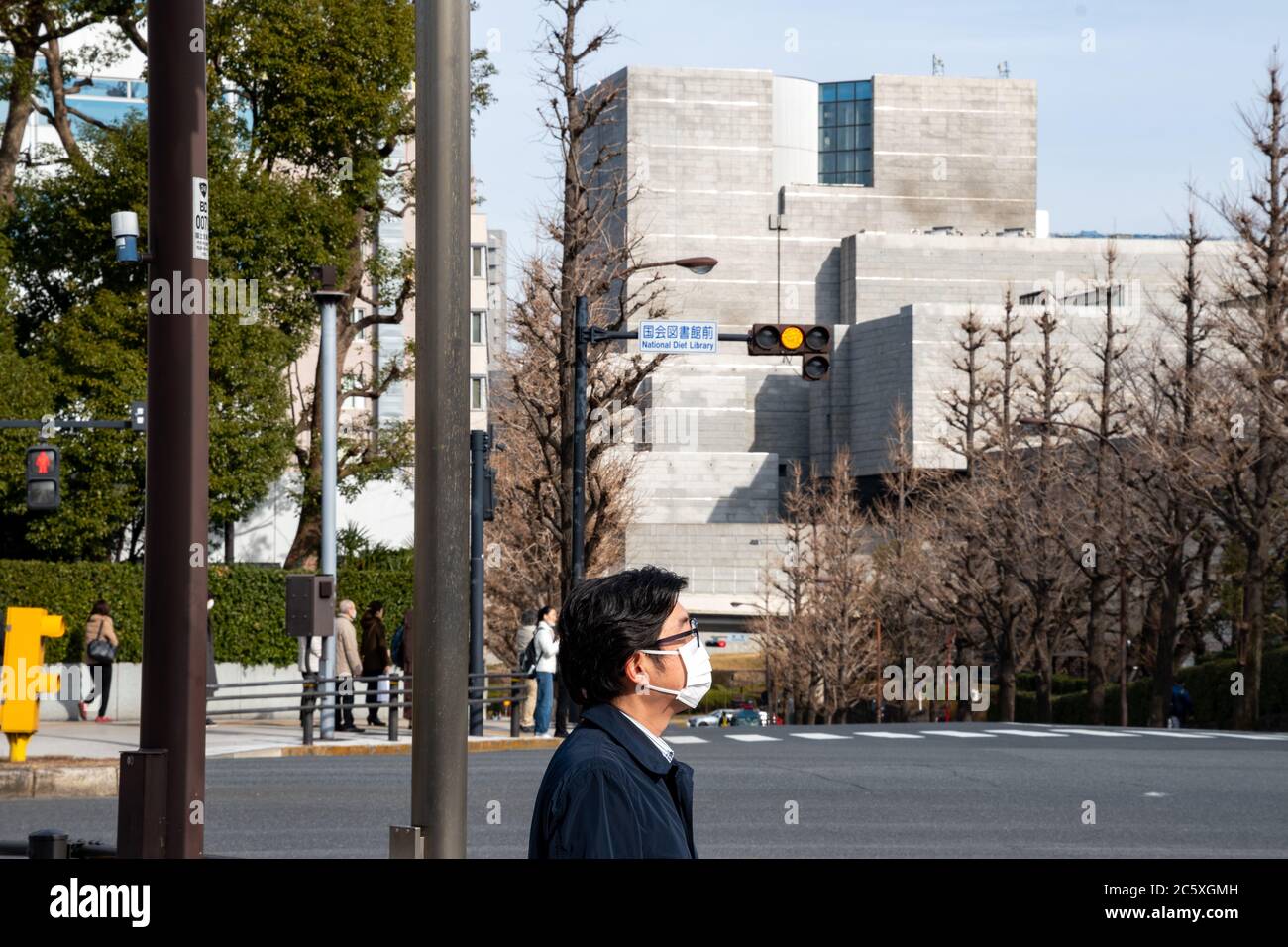 A man wearing a face mask at a crossroad next to the National Diet Library and the National Diet Building (Kokkai-gijidō).Tokyo, Japan Stock Photo