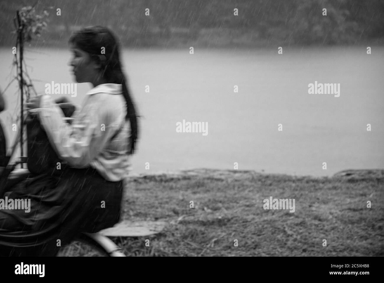 Blurred young female student on a bicycle on a rainy day in Angkor Wat temple area. Siem Reap, Cambodia. Stock Photo