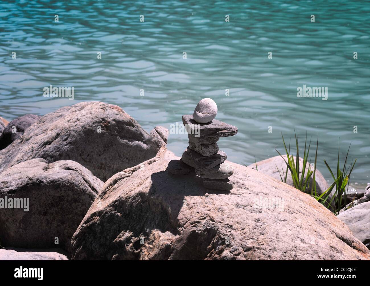 Inukshuk, piled stone structure over rocks with lake view behind. Relax Stock Photo