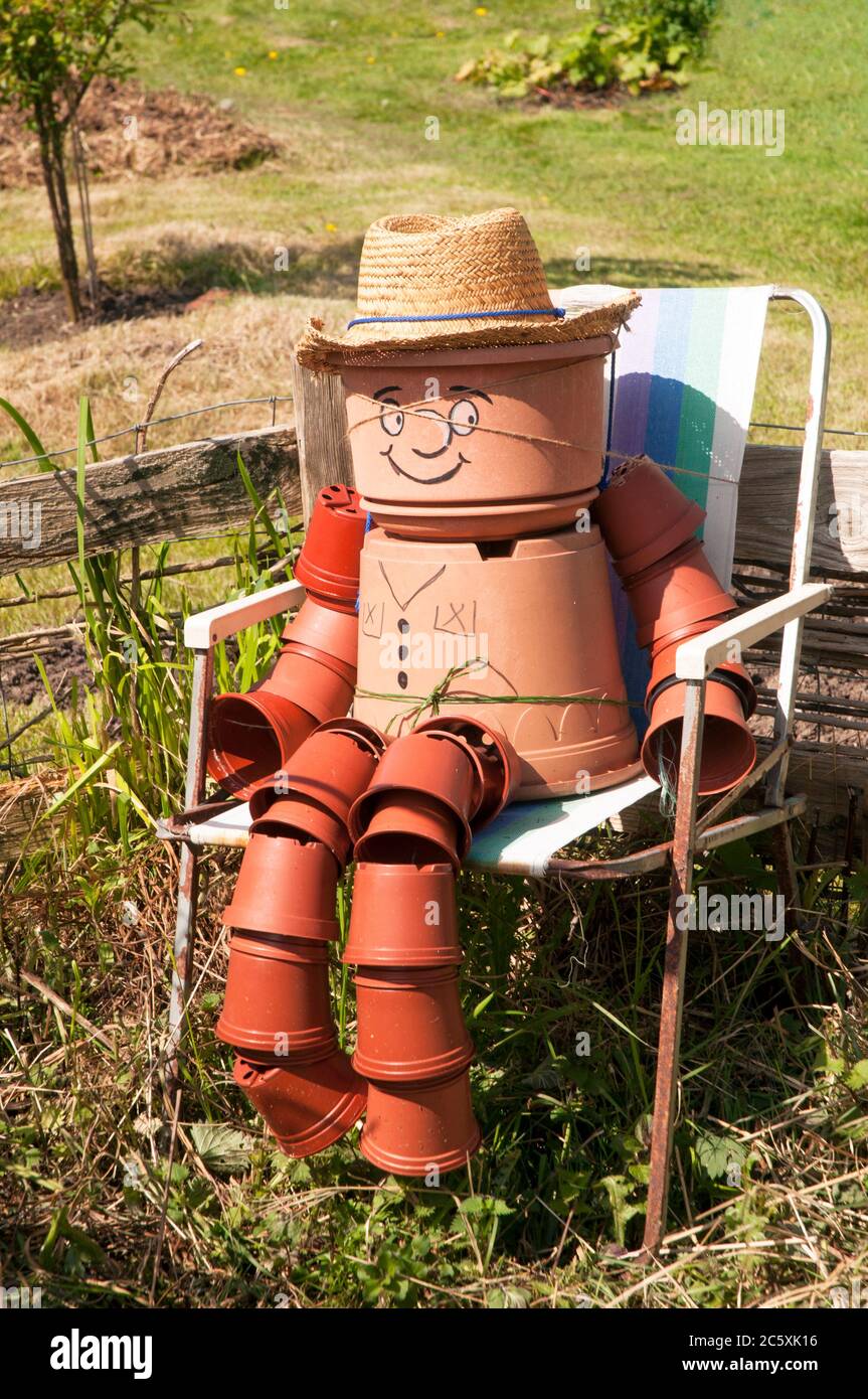 Plantpot man on an allotment site sitting on a chair on a sunny day. All of the figure is made from different sized plant pots Stock Photo