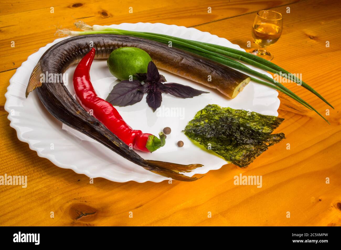 smoked garfish with lime, Basil, green onions, chili, nori chips, spices, olive oil in a white ceramic dish, on a wooden table Stock Photo