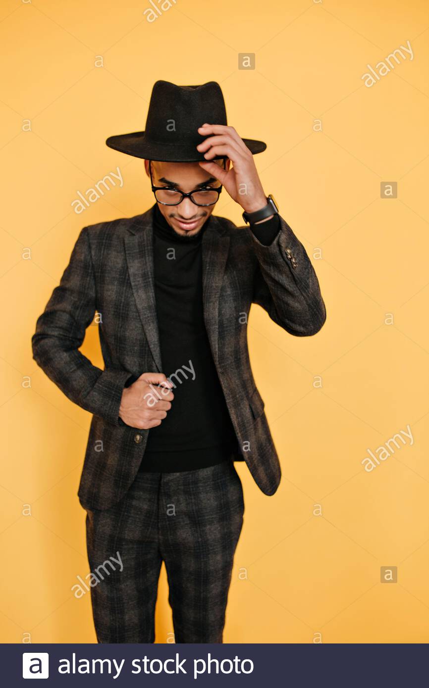 Indoor Portrait Of Glad African Male Model Playfully Posing On Yellow Background Confident Black Young Man In Jacket Touching His Hat During Photoshoot Stock Photo Alamy