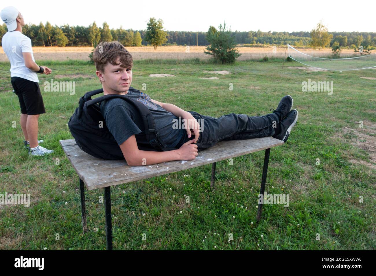 Young Polish teen enjoying a rest on a table with older brother behind flying a kite in their yard. Zawady Gmina Rzeczyca Poland Stock Photo