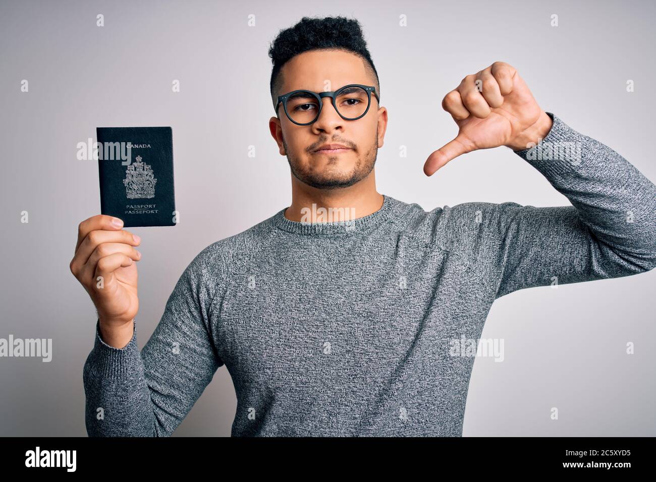 Young handsome tourist man on vacation wearing glasses holding Canada Canadian passport with angry face, negative sign showing dislike with thumbs dow Stock Photo