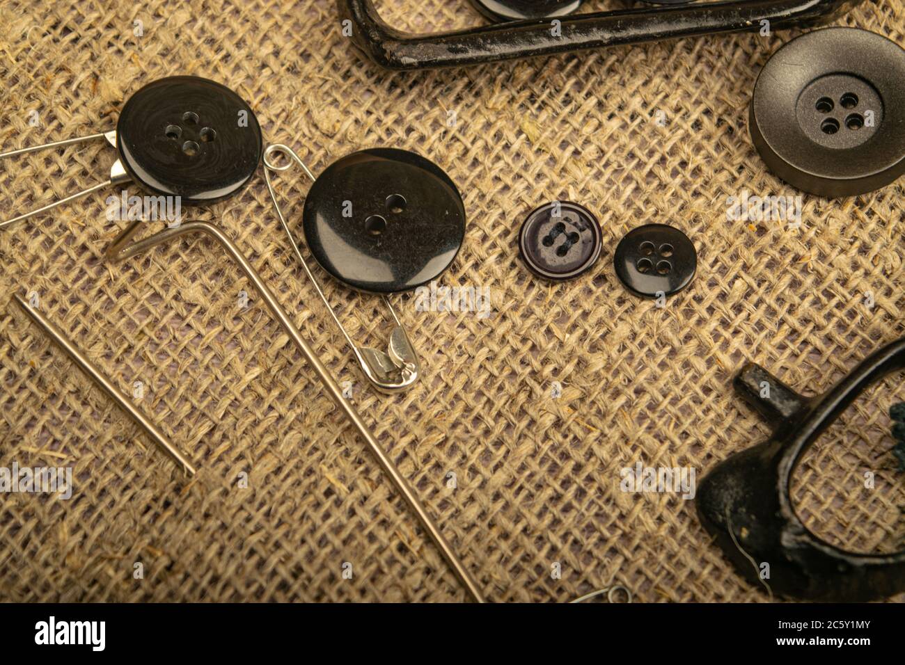 Pins of various sizes, tailor's scissors, and various buttons on coarse-textured burlap. Close up Stock Photo