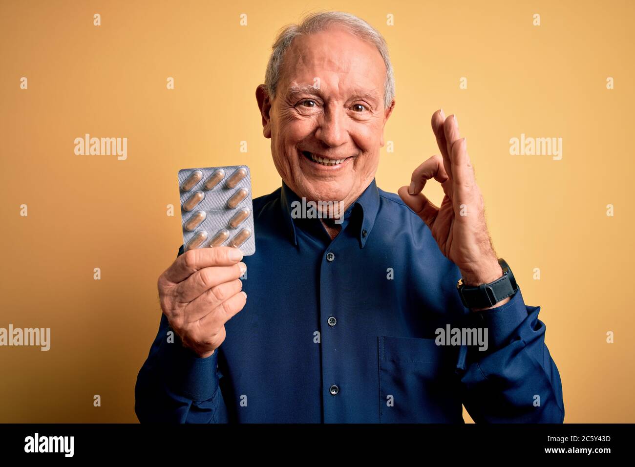 Senior grey haired man holding pharmaceutical pill drugs over yellow ...