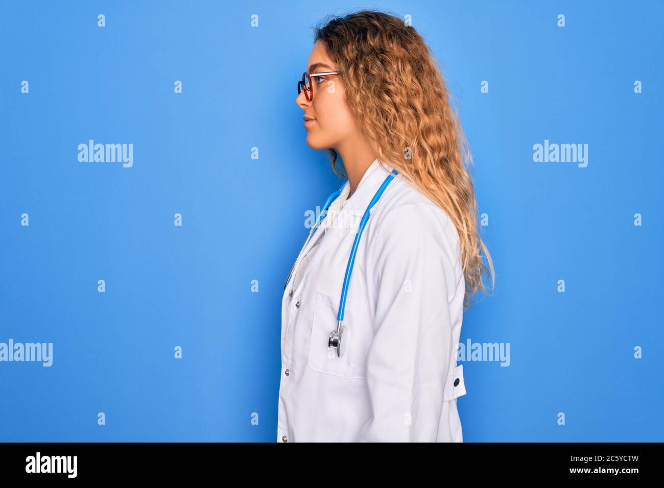 Young beautiful blonde doctor woman with blue eyes wearing coat and ...