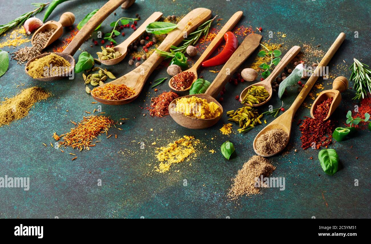 Various spice and dried herbs on dark green background. Top view of spices in wooden spoons Stock Photo