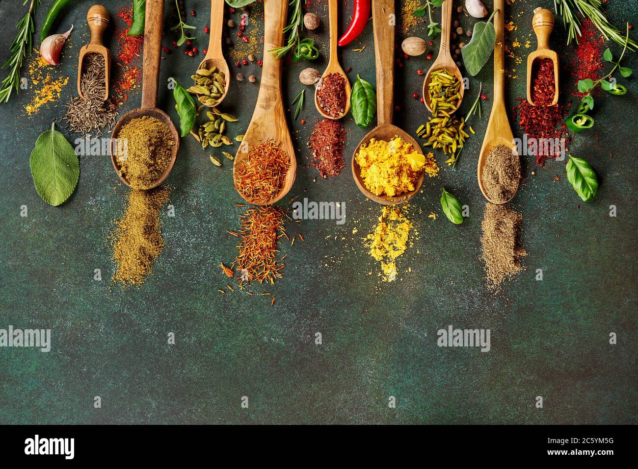 Various spice and dried herbs on dark green background. Top view of spices in wooden spoons Stock Photo