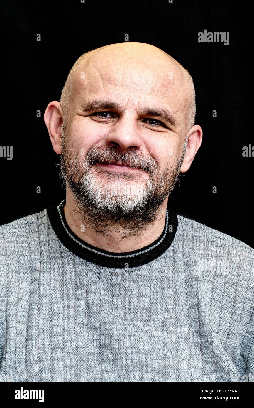 middle-aged bald bearded man smiling on black background Stock Photo