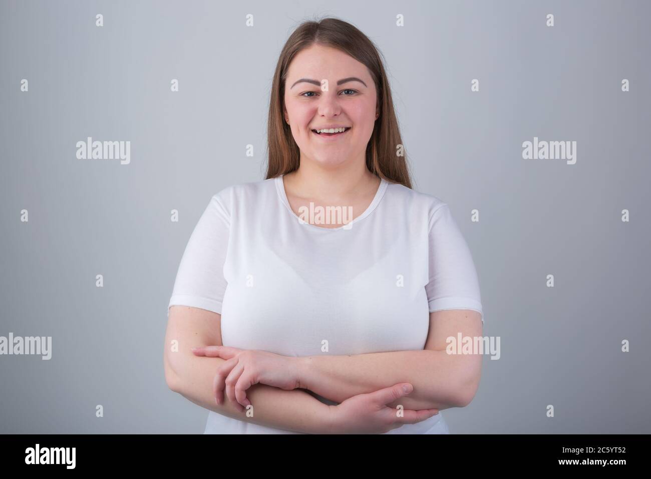 Happy plus size girl.Beautiful overweight young woman in early 30s posing in studio with friendly smile and crossed hands wearing casual white t-shirt Stock Photo