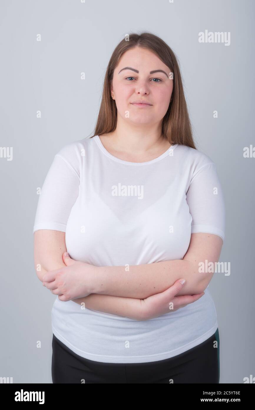 Beautiful chubby girl in 30s posing in studio wearing casual white t-shirt with crossed hands,looking in camera.Pretty young plus size woman pose with Stock Photo