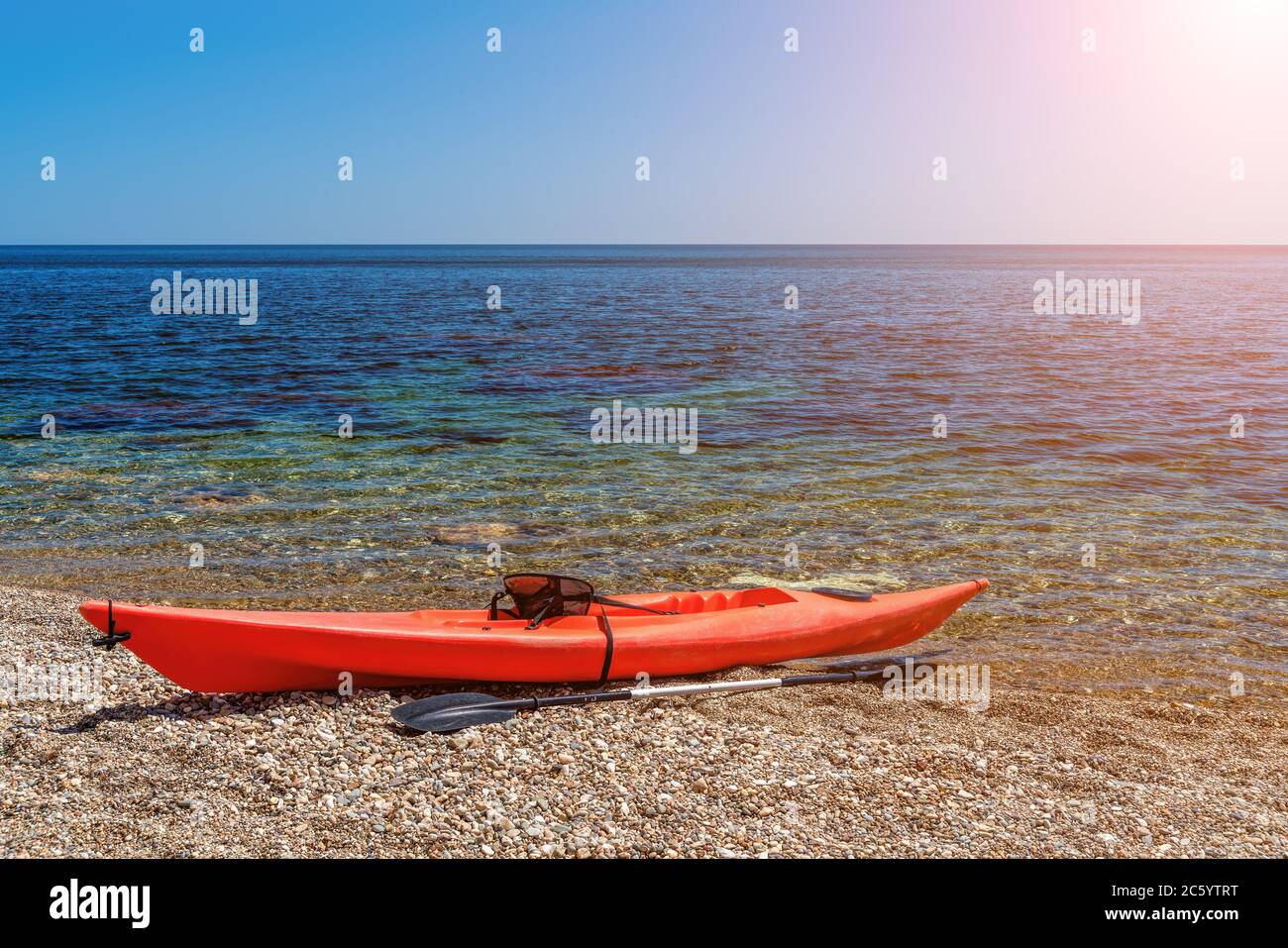 Red kayak on an isolated rocky beach, against the background of a the sea. The concept of an active life in harmony with nature. Stock Photo