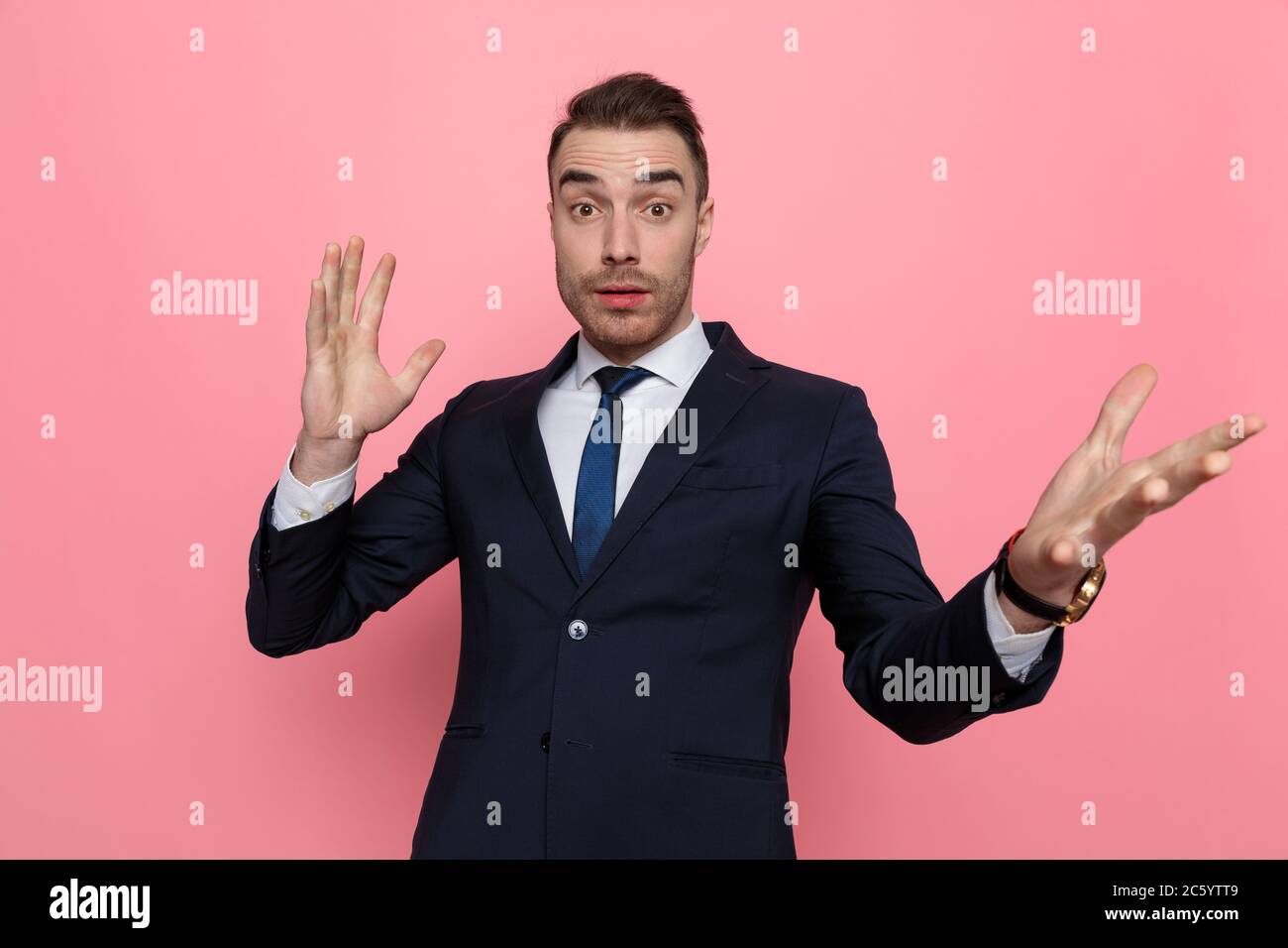 confused young businessman holding hands up and gesticulating, standing on pink background Stock Photo