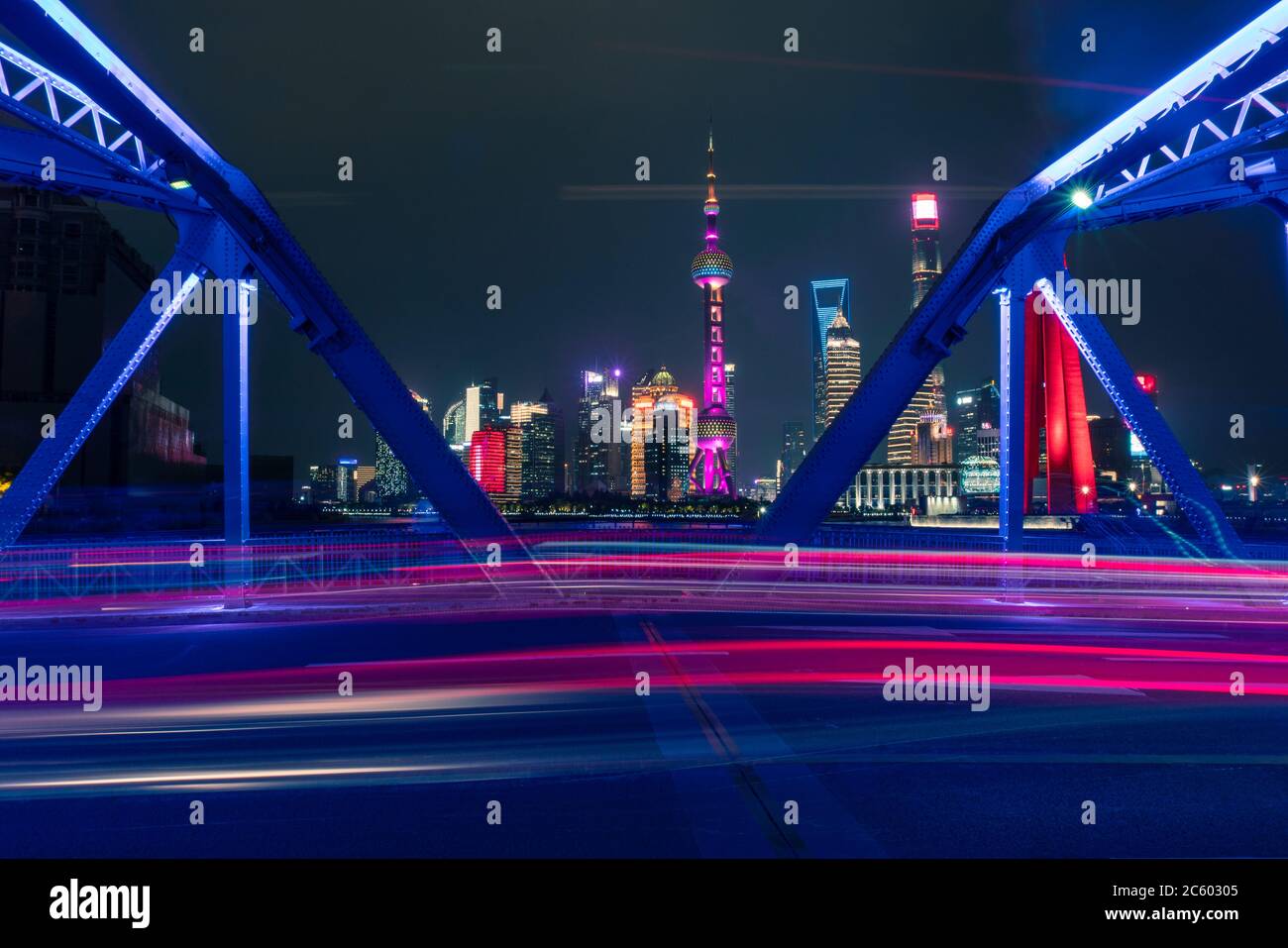 Night view of Waibaidu Bridge, a landmark steel bridge in Shanghai, with traffic and modern skyscrapers in the back. Stock Photo