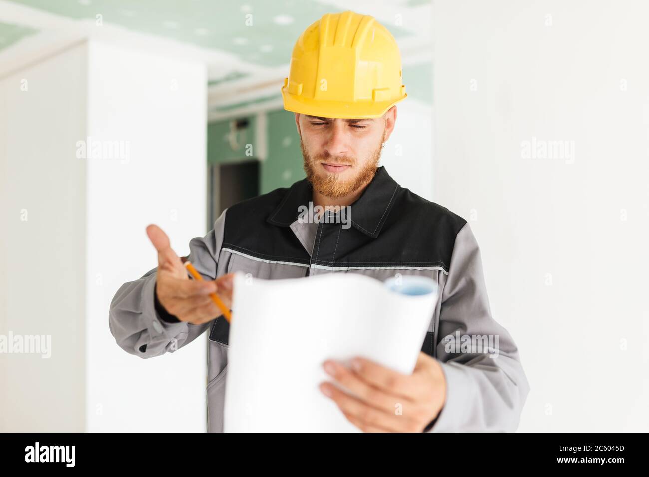 Young serious engineer in work clothes and yellow hardhat though Stock Photo