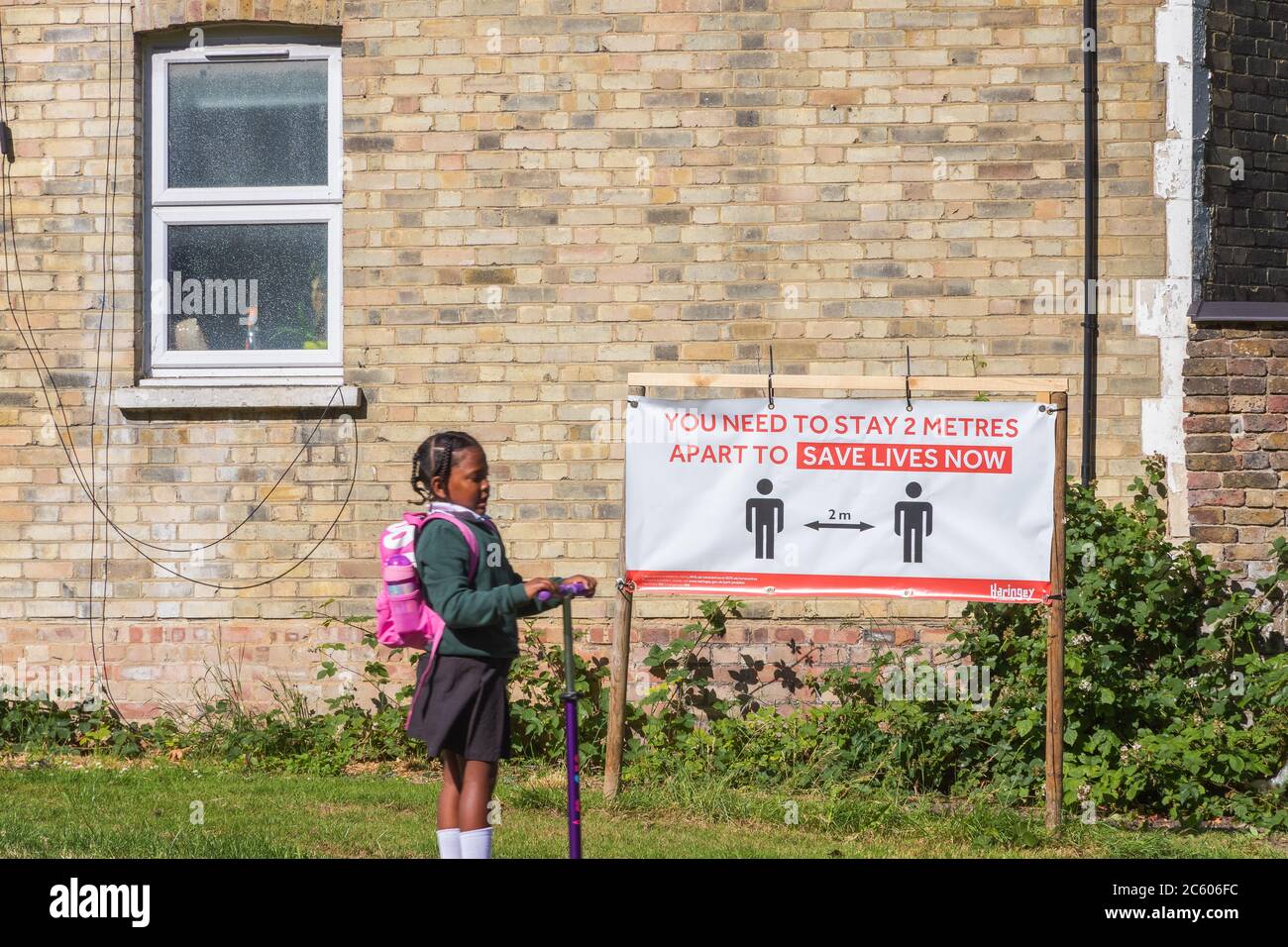 London, UK - 16 June, 2020 - Social distancing sign with an indication of 2 metres distance in a park with a girl riding a scooter through Stock Photo