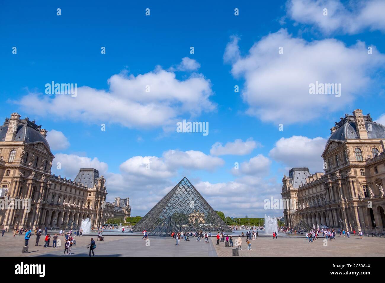 France. Sunny summer weather in Paris. The famous courtyard of the Louvre Museum and the glass pyramids. Many tourists. Clouds Stock Photo