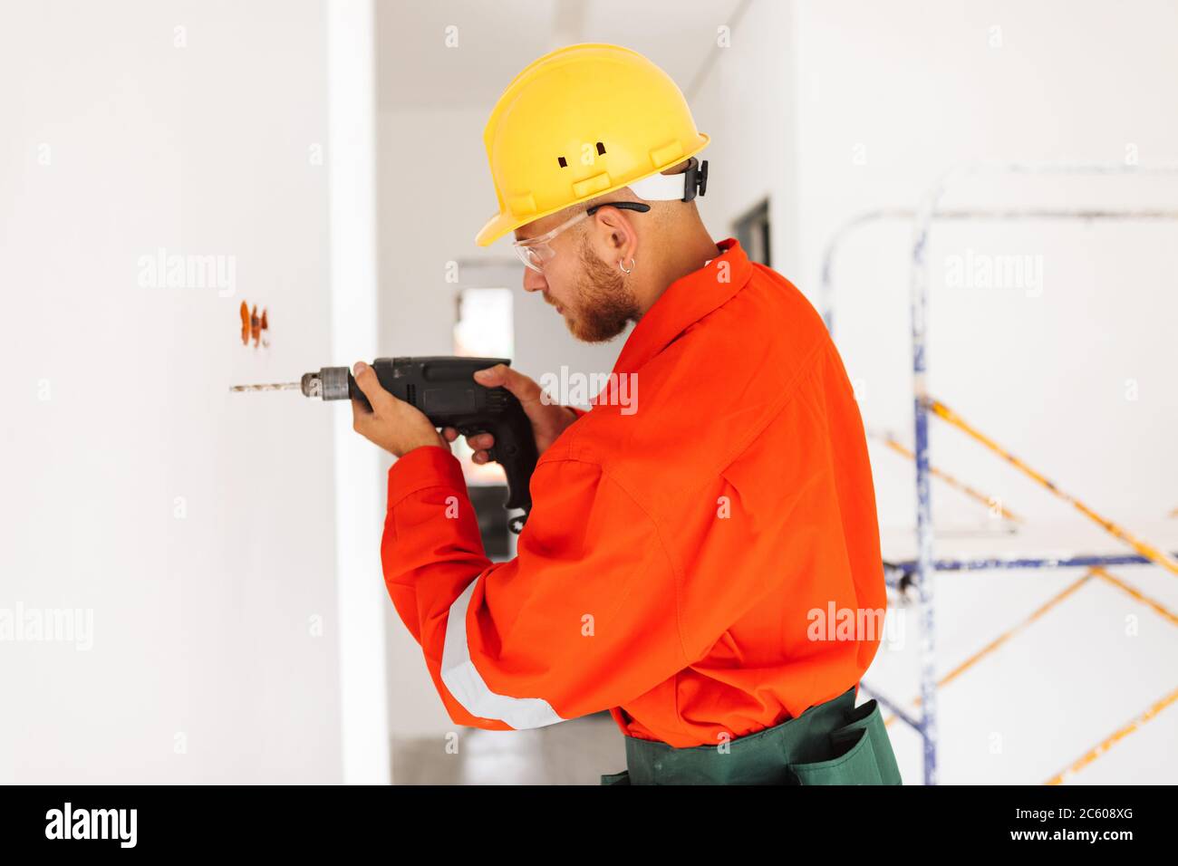 Young foreman in orange work clothes and yellow hardhat using el Stock Photo