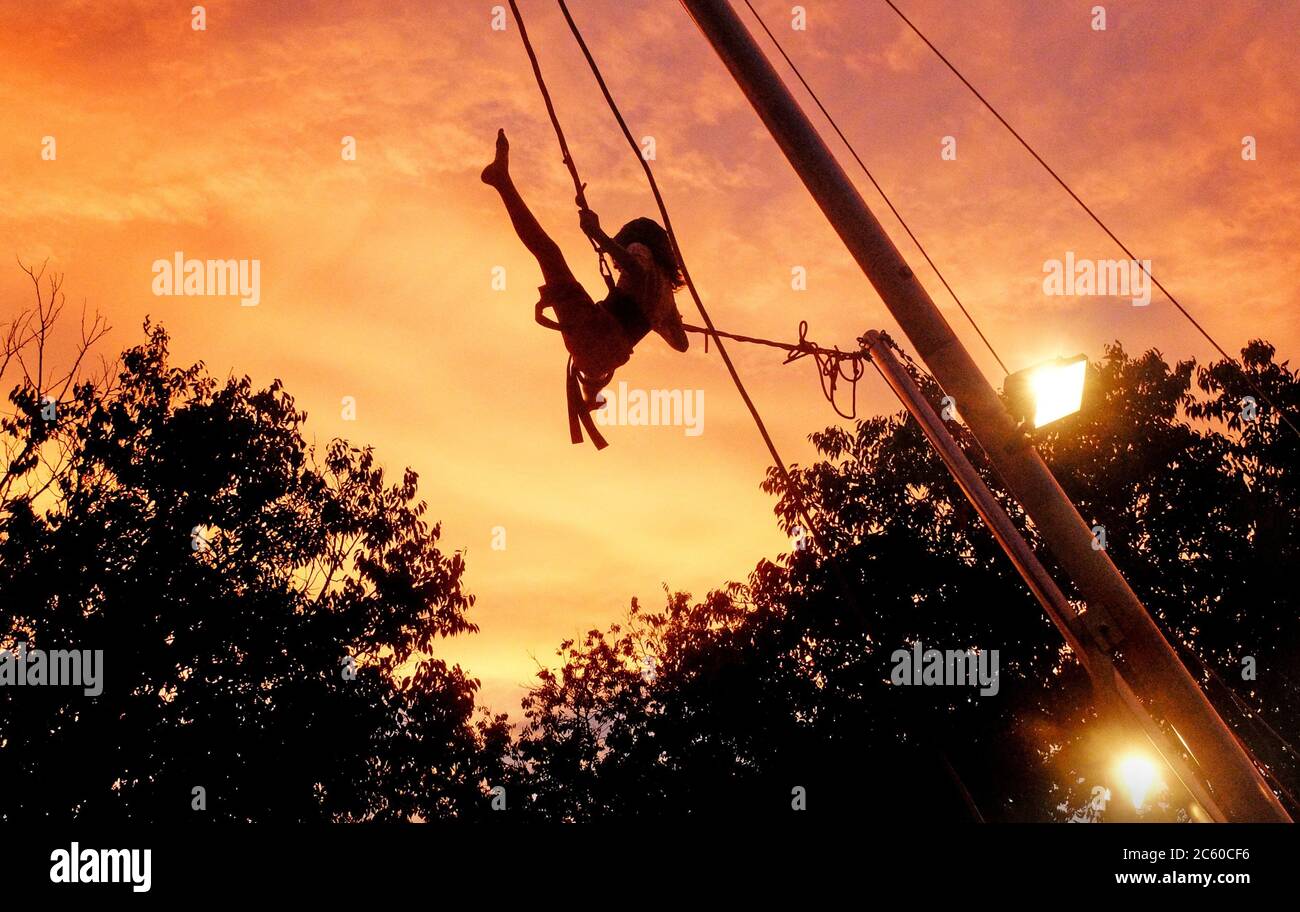 A young girl pumps her legs high in the air to push her rope swing high into the air of an evening sunset, South of France near Pezenas, Stock Photo