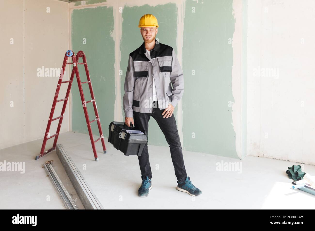 Smiling engineer in work clothes and yellow hardhat holding tool Stock Photo