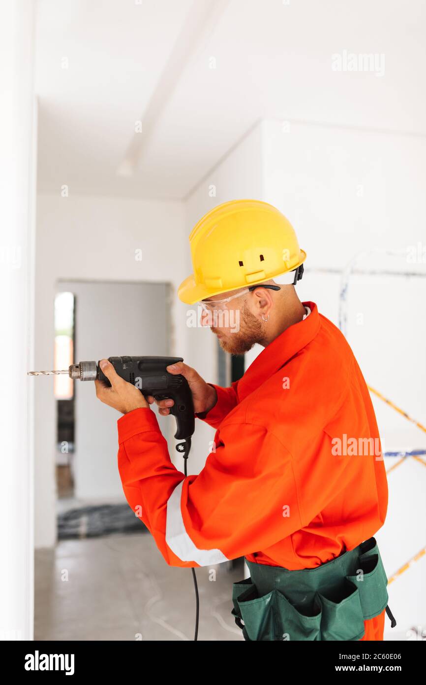 Young builder in orange work clothes and yellow hardhat using el Stock Photo