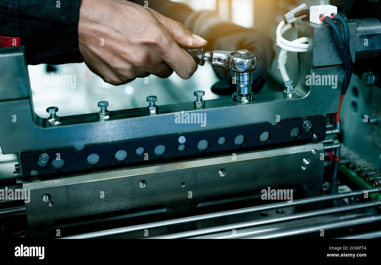 Mechanic technician hand fixing industrial machinery in factory. Professional technician service and maintenance packing machine equipment. Worker use Stock Photo