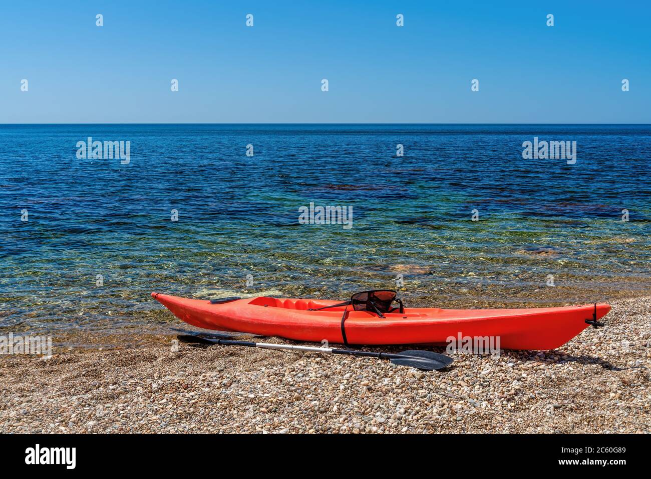 Red kayak on an isolated rocky beach, against the background of a the sea. The concept of an active life in harmony with nature. Stock Photo