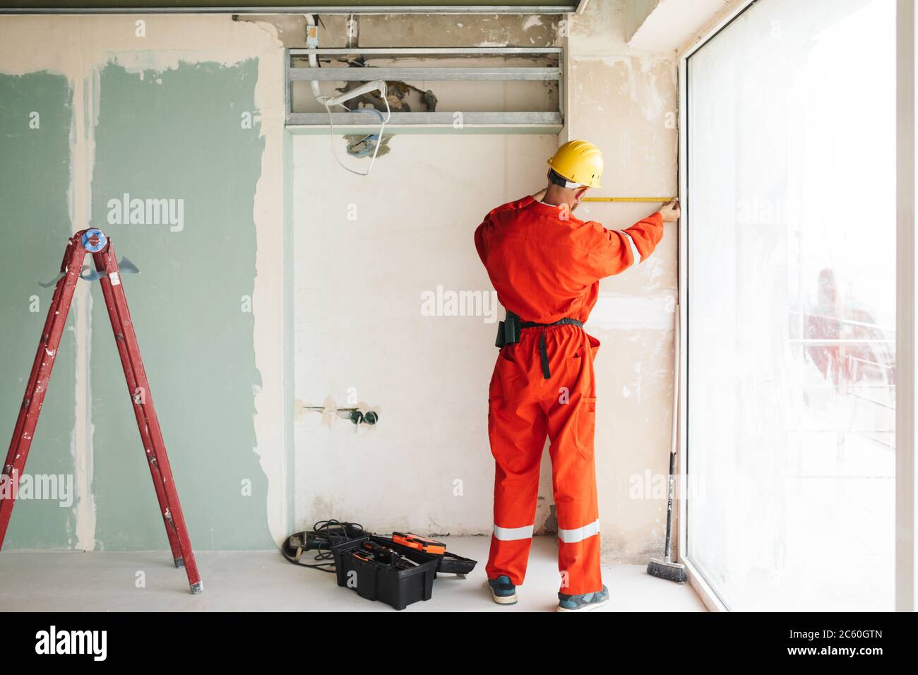 Builder in orange work clothes and hardhat using measuring tape Stock Photo