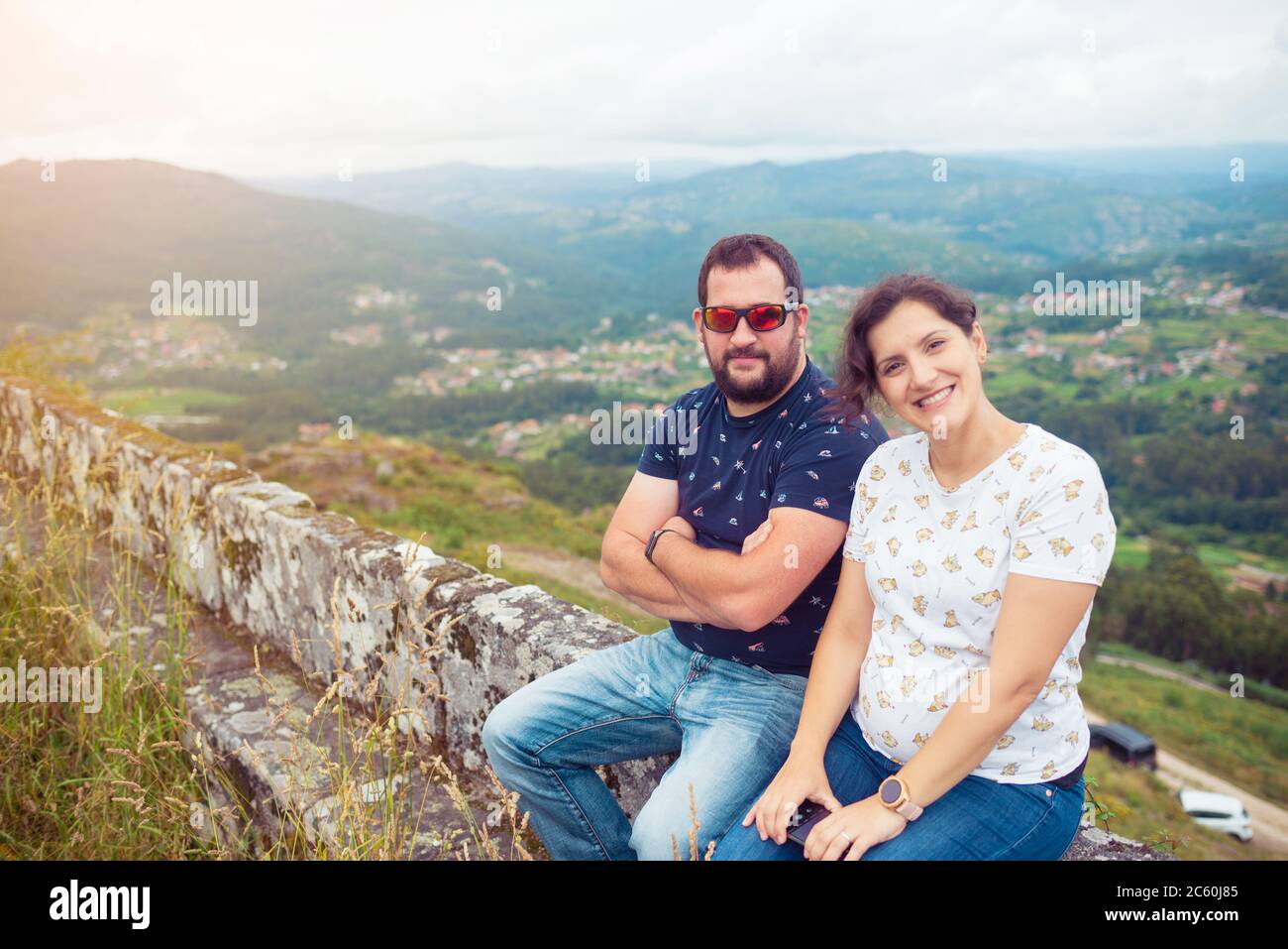 Pregnant heterosexual couple posing in front of a beautiful landscape with mountains and forests Stock Photo