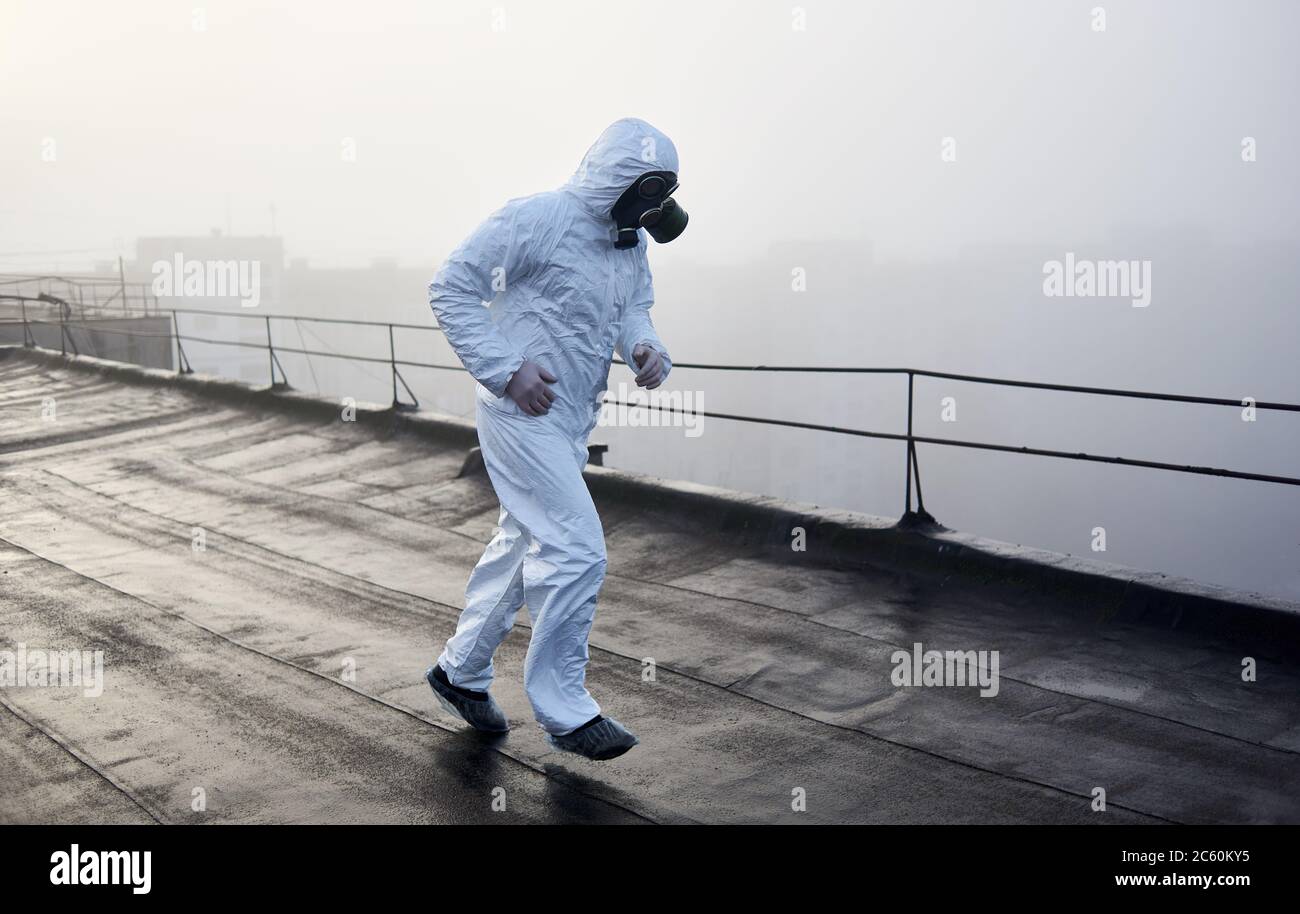 Man wearing white coverall and gas mask, running on the roof of an