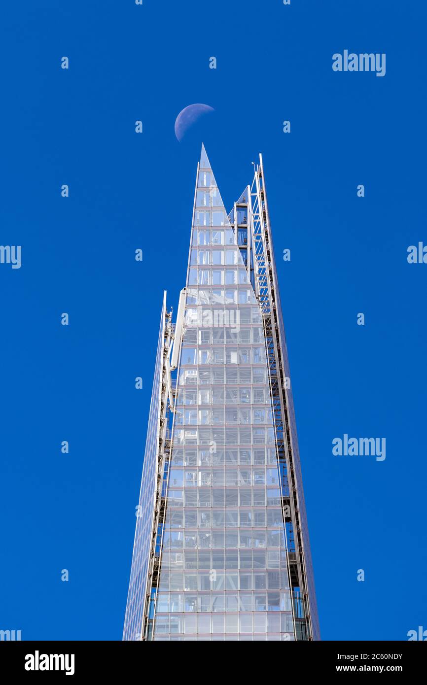 View of the uppermost part of the Shard with a quarter moon in a clear blue sky Stock Photo