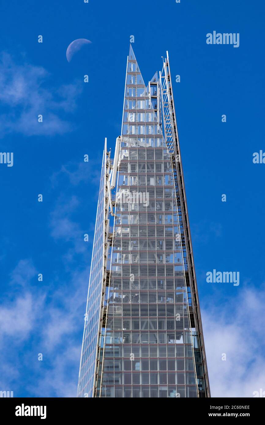 View of the uppermost part of the Shard with a quarter moon in a blue sky with light clouds Stock Photo