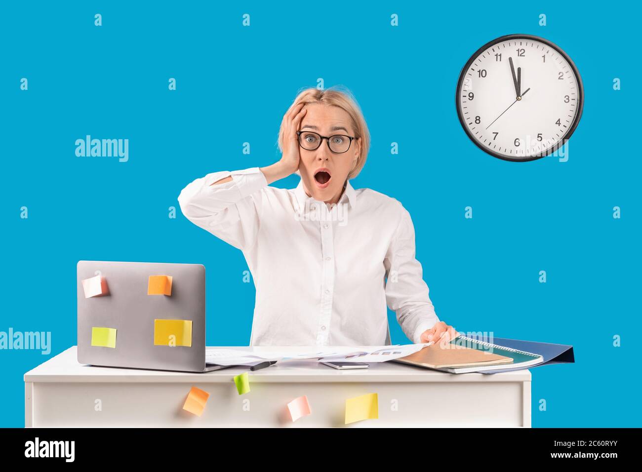 Office time management. Terrified company employee missing deadline at her desk with laptop, blue background Stock Photo