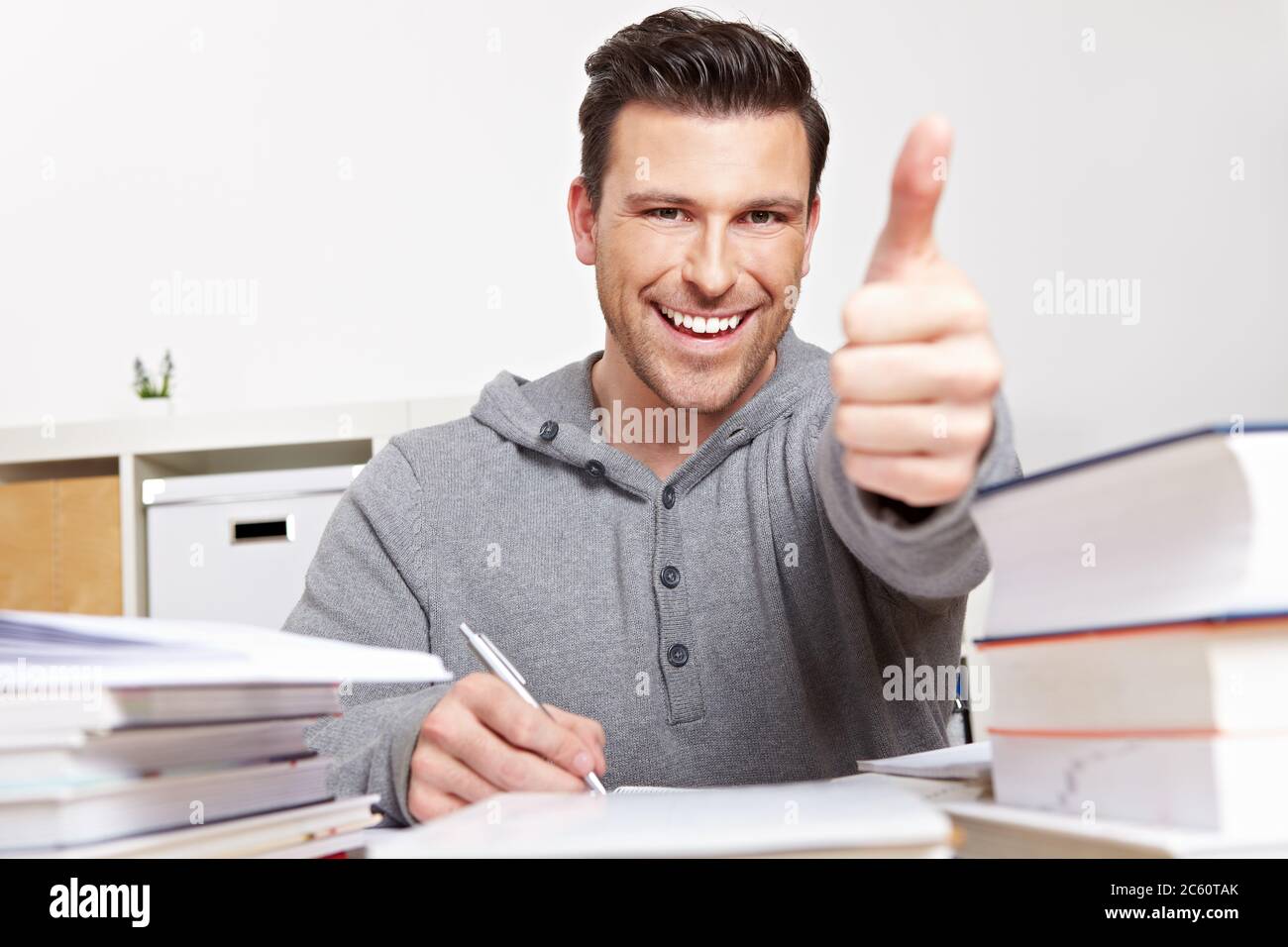 Student holds thumbs up while studying with lots of books Stock Photo ...