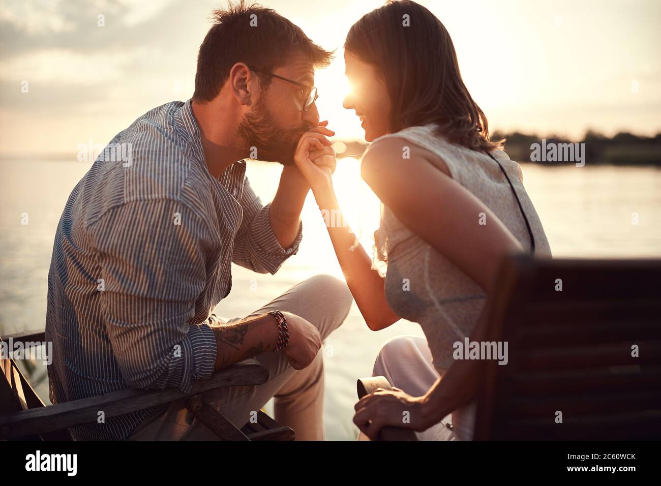 close up of young beardy man holding and kissing hand of a woman beside the  river at sunset Stock Photo