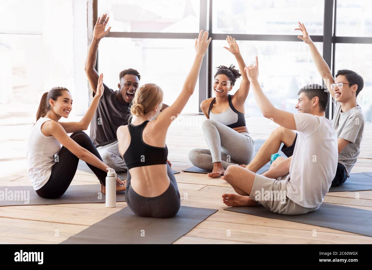 Motivated Multiracial Friends Voting With Raised Hands After Training In Yoga Studio Stock Photo