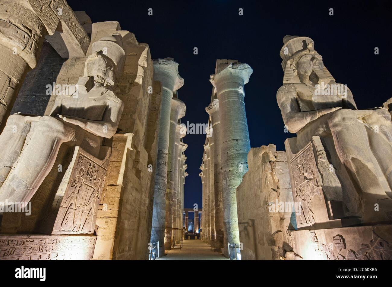 Large statues of Ramses II with columns in hypostyle hall at ancient egyptian Luxor Temple lit up during night Stock Photo