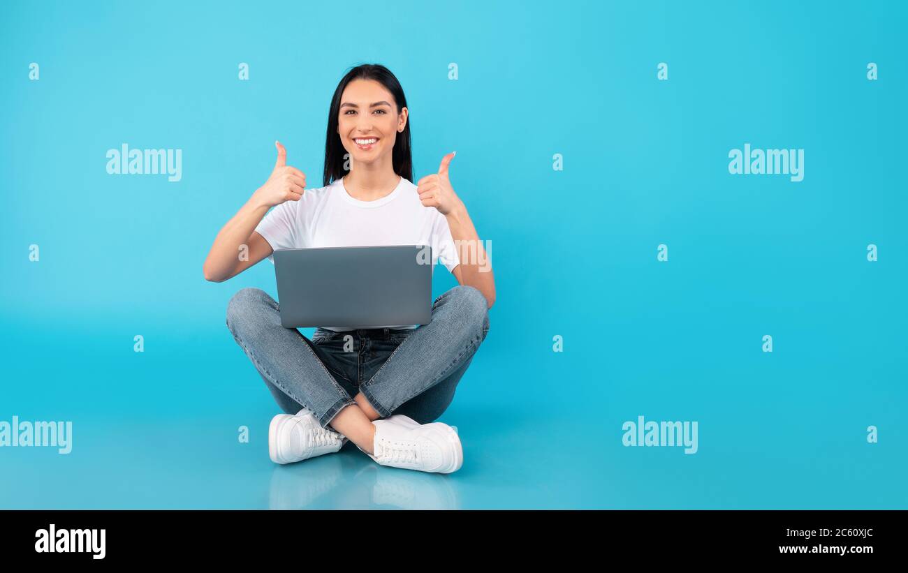 Happy lady sitting with laptop showing thumbs up Stock Photo - Alamy