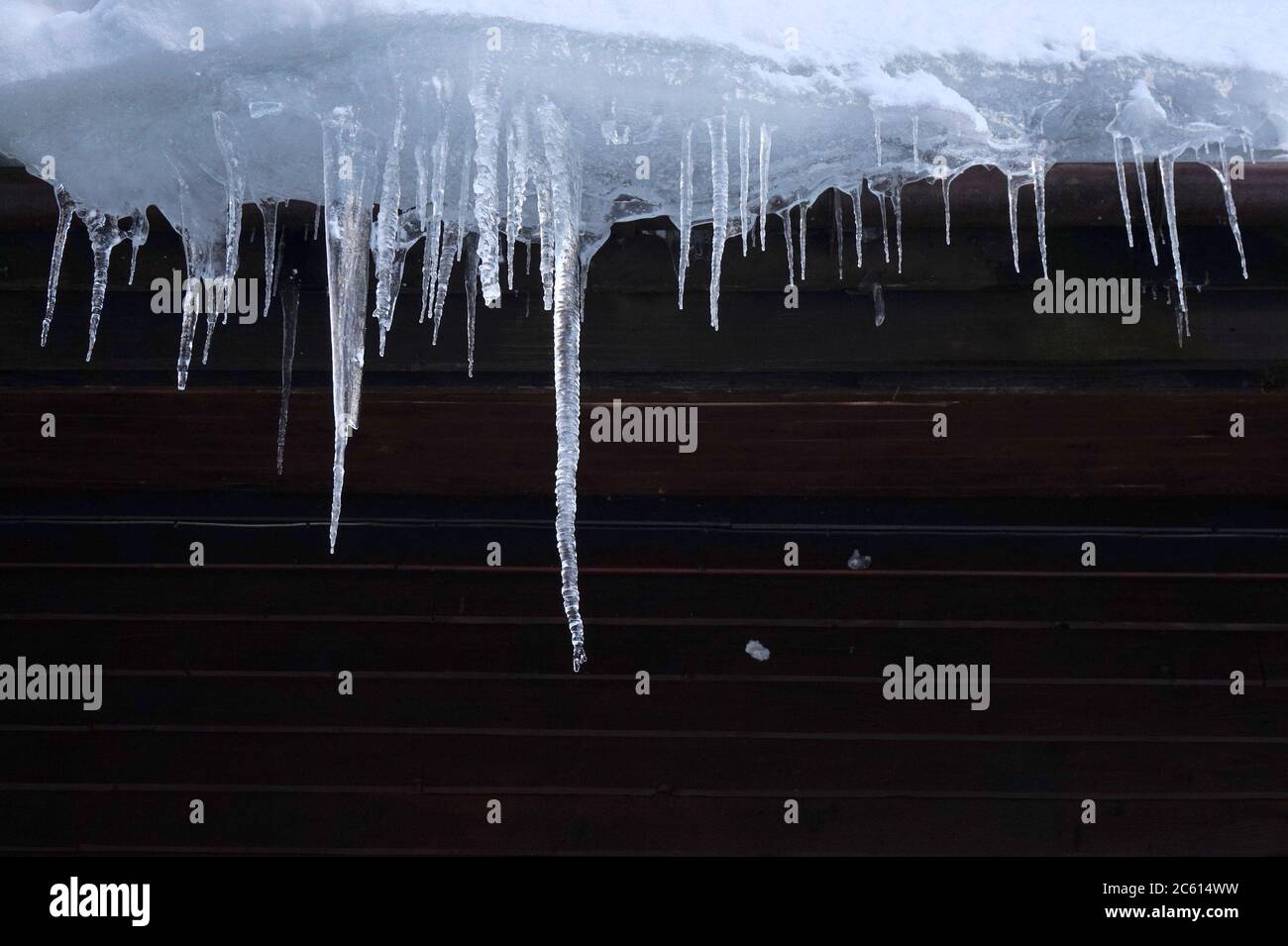 Wooden cabin roof icicles in winter. Icicles signify insufficient building insulation and thermal losses. Stock Photo