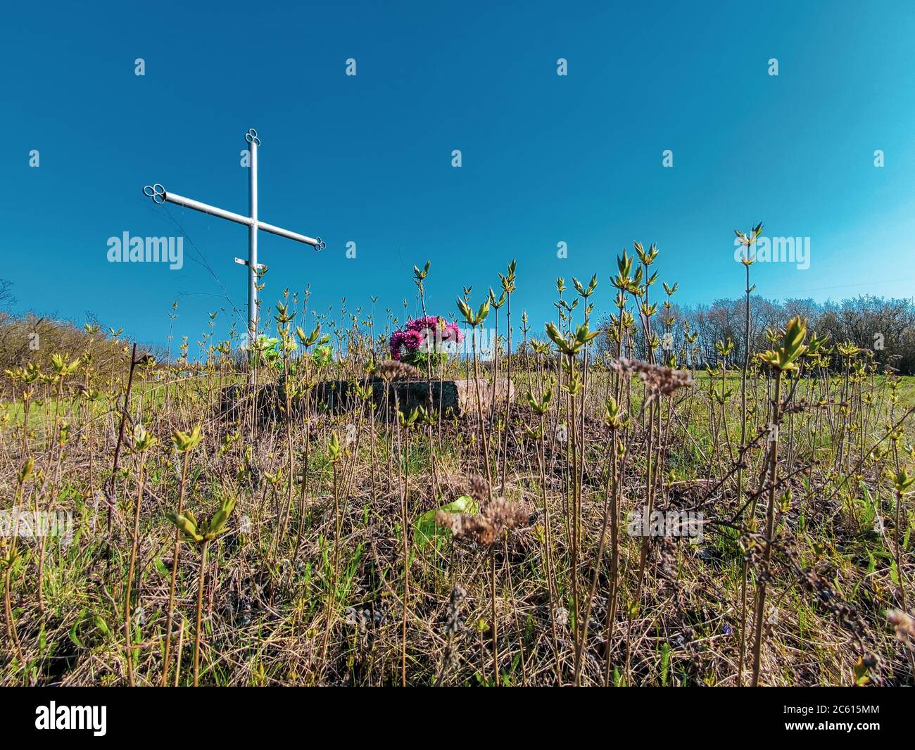 Aged cross tomb with flowers and overgrown grass. wake old christian traditional Stock Photo