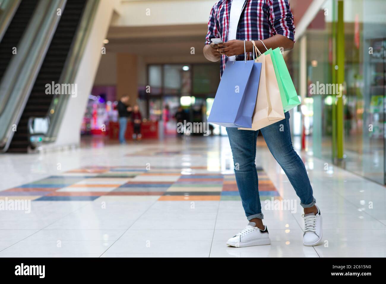 Black guy with shopping bags using cellphone in mall, messaging with friends Stock Photo