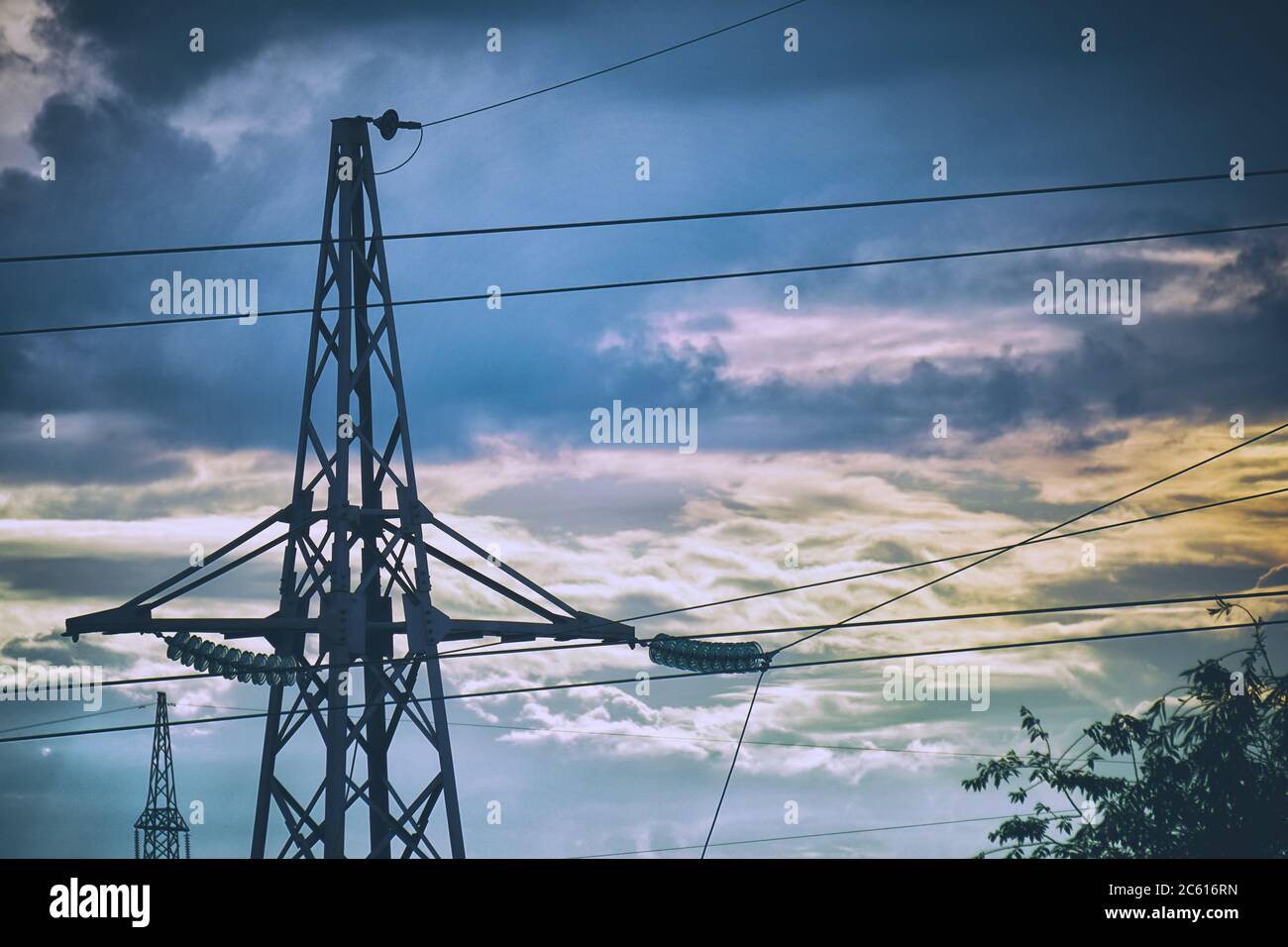 Silhouette of a high-voltage power line tower against a cloudy sky in ...