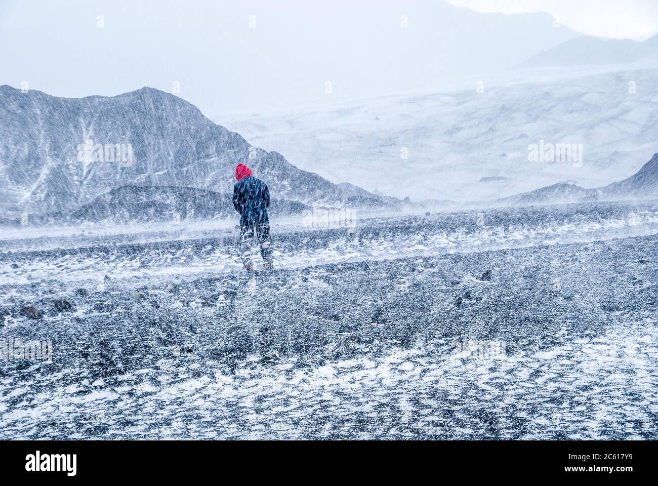 Man walking into a storm in a bleak landscape with hail, ice, snow near glacier on Iceland Stock Photo