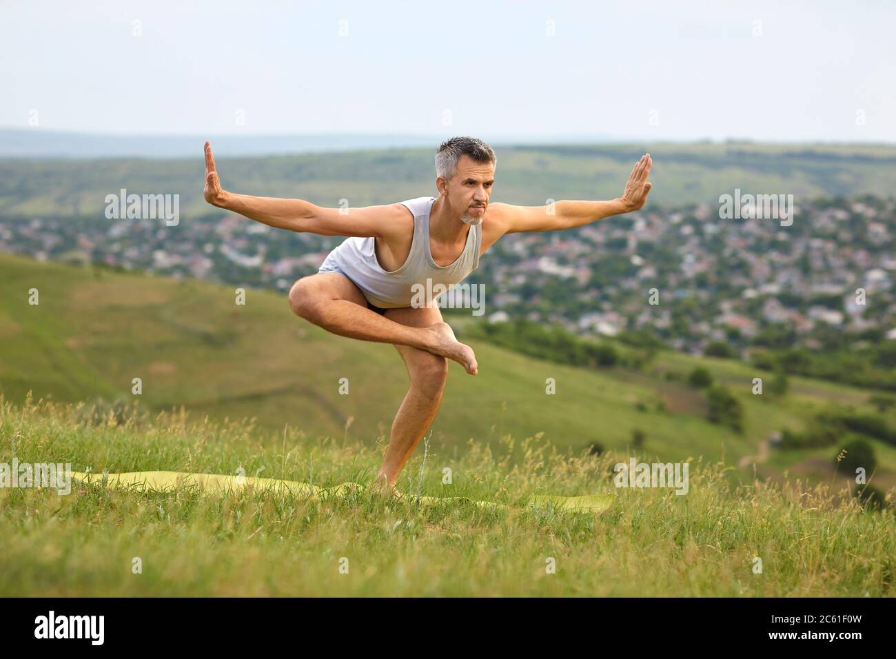 Sporty man doing yoga practice on mountain top. Peaceful guy enjoying his training surrounded by beautiful nature Stock Photo